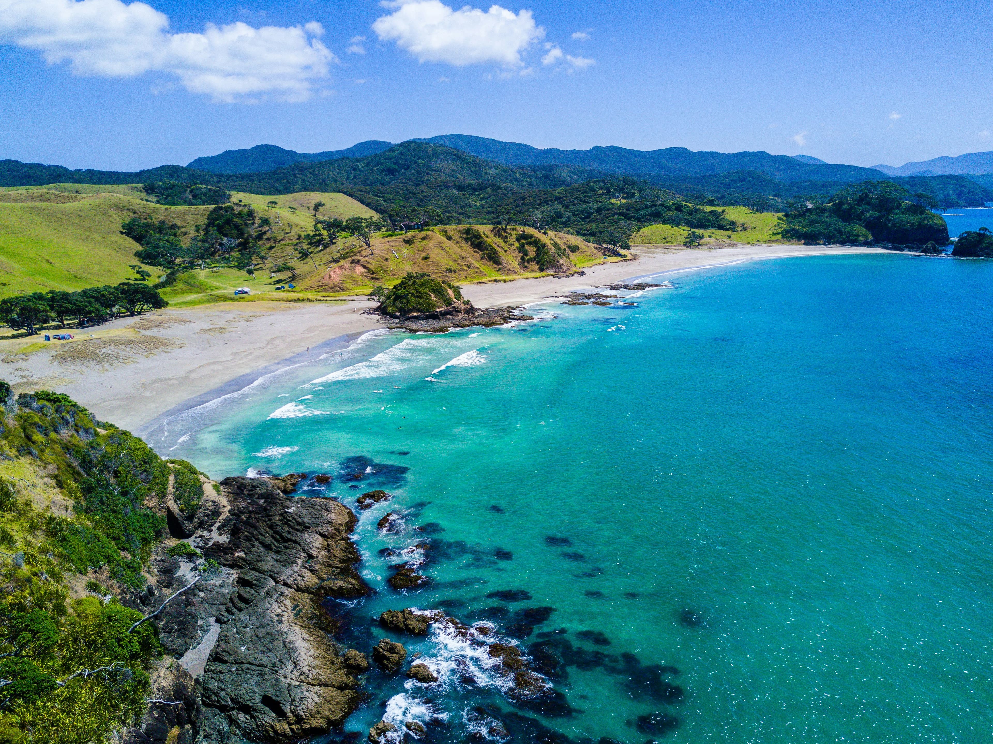 Aerial view of a Northland coast with turquoise water and rolling green hills. Photo by Rod Long.